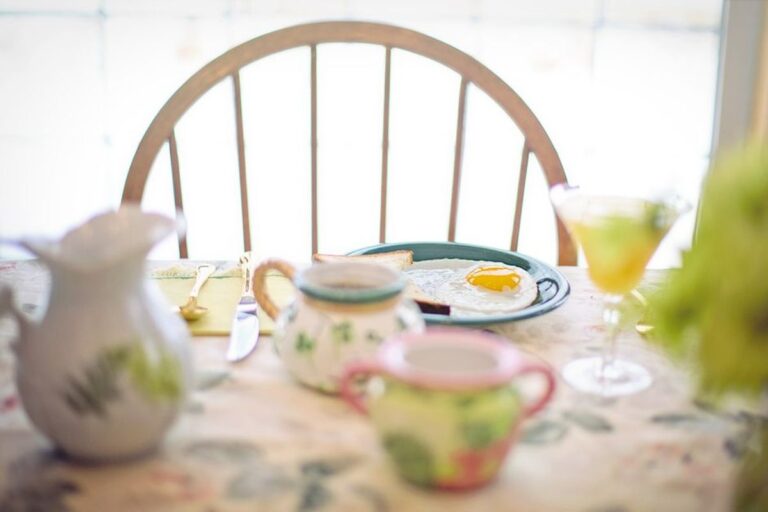 Une table de petit-déjeuner dressée devant une chaise vide, vaisselle claire
